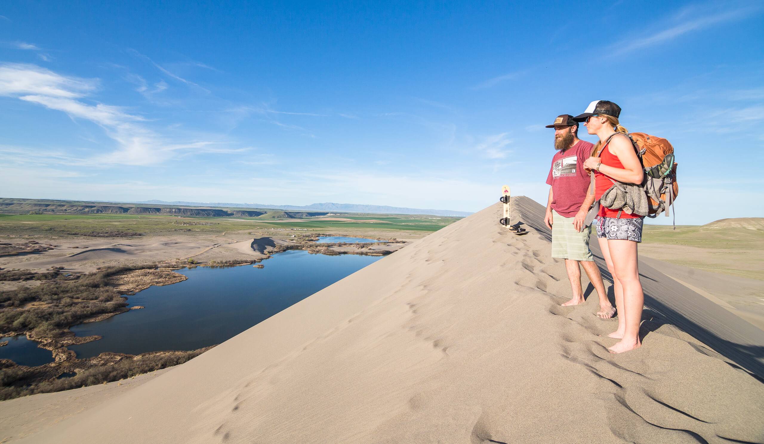 Two people standing on the top of a sand dune.