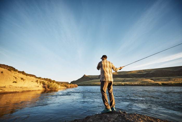 A man fishing along a river at sunset.