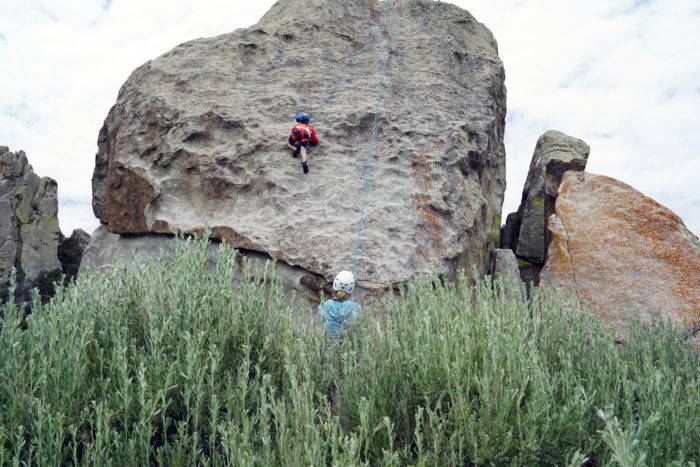 Young boy climbing a large rock in climbing gear