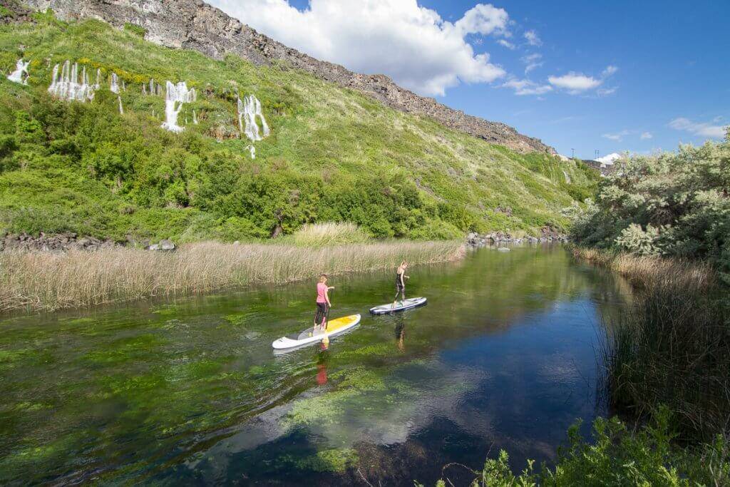 Two women paddle boarding in a river.