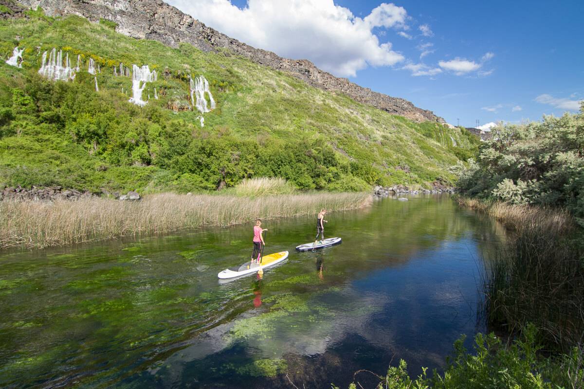 Two women paddle boarding in a river.