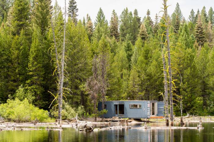 Old shipping container turned into a cabin on the side of a lake.