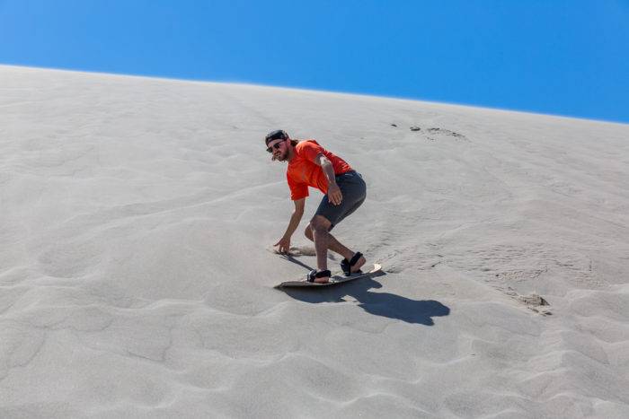 man sandboarding on a sand dune.