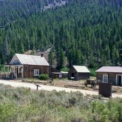 Various historic buildings at the base of a tree-covered mountain at Custer Ghost Town.