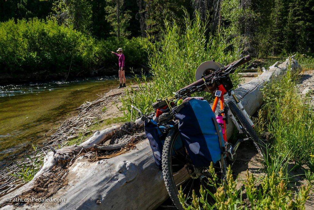 woman fishing on mountain river with mountain bike in foreground