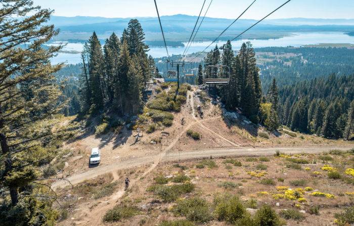 mountain bike riders stand beneath mountain lift.