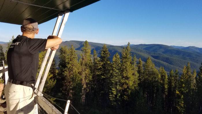 man looking out over forest from fire lookout