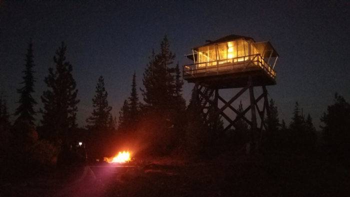 A fire lookout with a campfire burning below