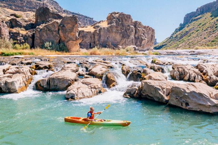 man in kayak near small set of waterfalls