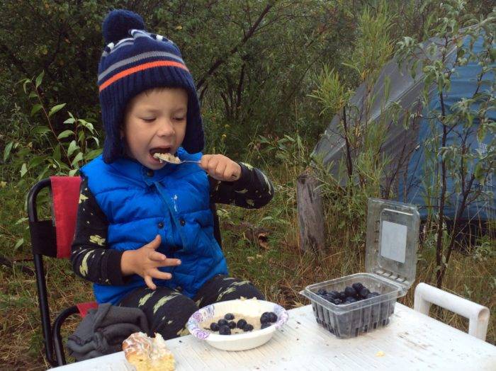 little boy eating oatmeal at a campsite