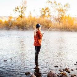 a woman in an orange plaid shirt fishing in the Boise River during fall.