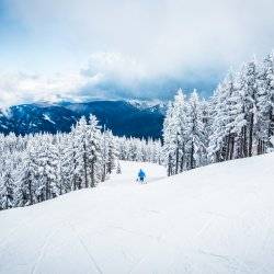 A person in outdoor gear skiing at Silver Mountain Resort surrounded by snowy peaks in the winter.