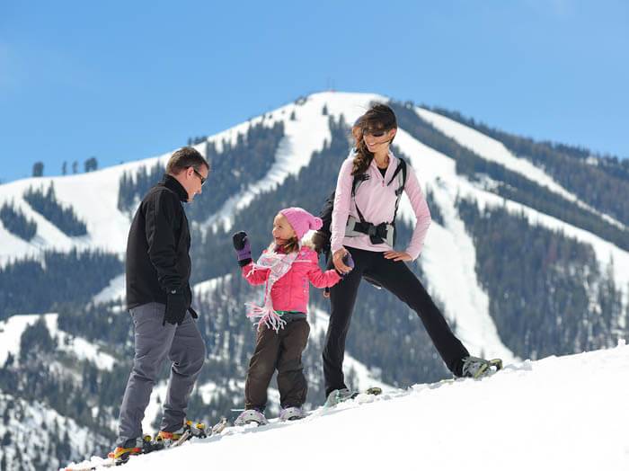 Two parents and their daughter stand on a snowy slope with snowshoes on.