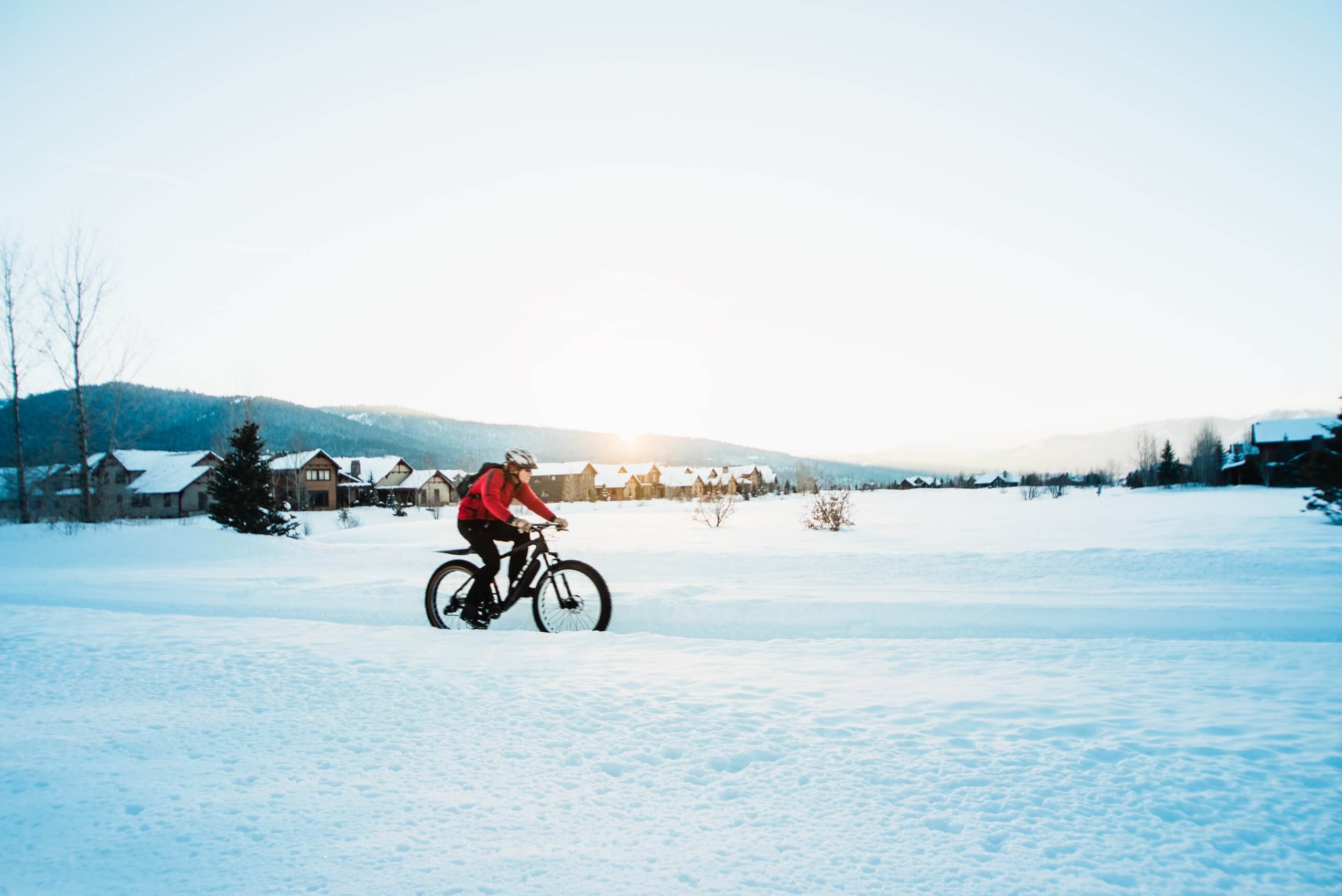 A man wearing a red jacket rides a fat tire bike through a snowy field in Victor, Idaho