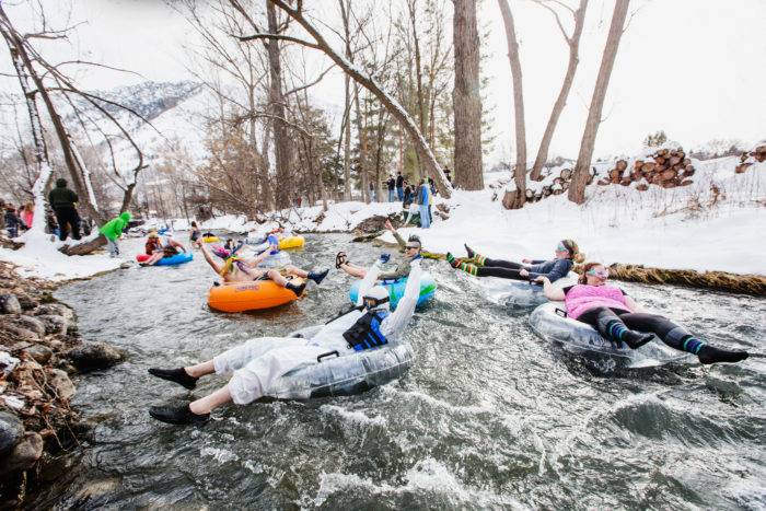 People floating on inner tubes down a river lined with trees and snow at the Fire and Ice Winterfest.