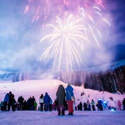 Several people watching fireworks at Schweitzer and snow-covered mountains and trees in the background.