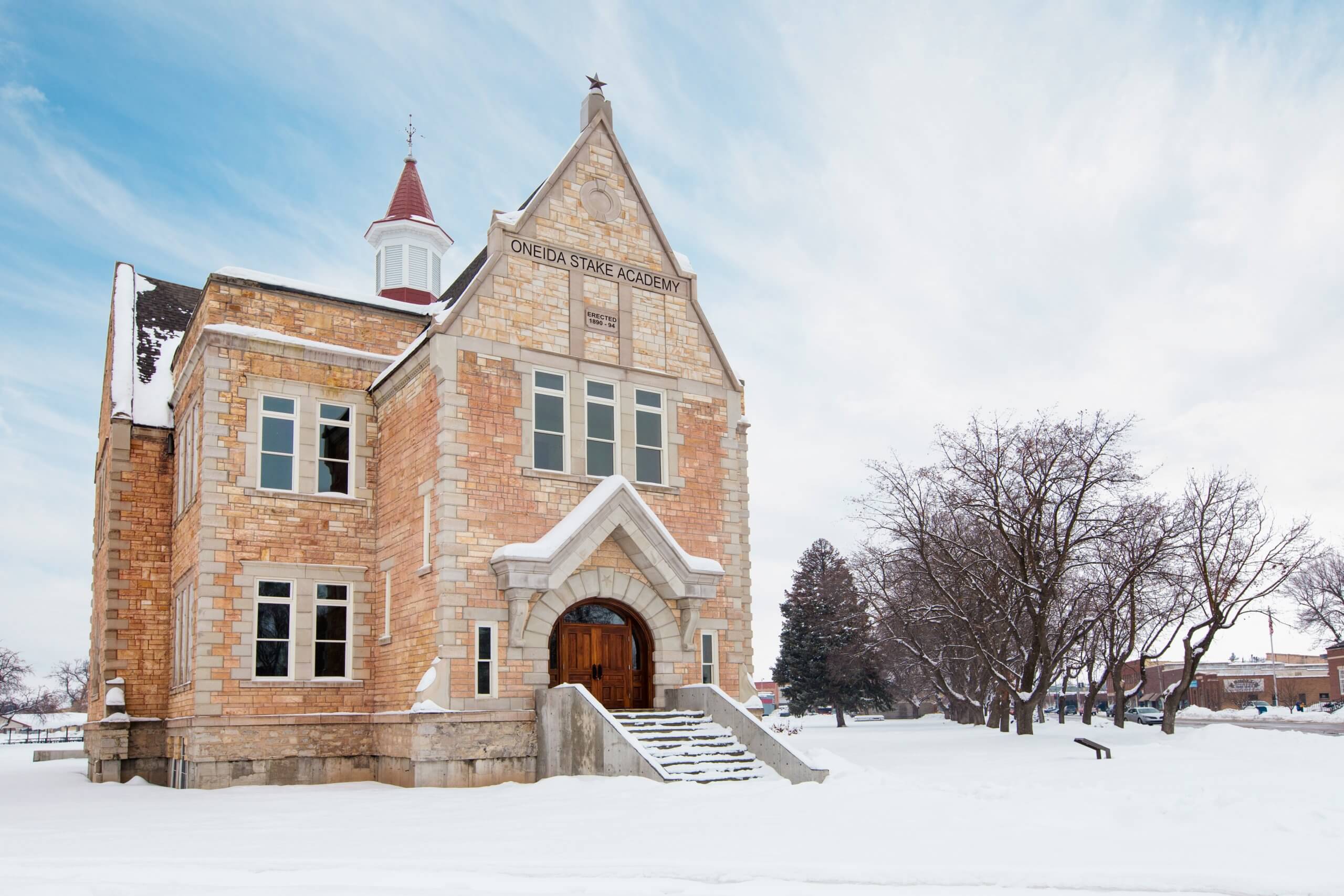 View of the historic, brick-builtOneida Stake Academy surrounded by a field of snow and bare trees.