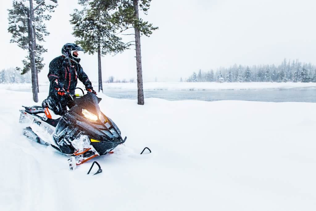 A person sits on a snowmobile at Island Park, Idaho with snow falling in the background. 