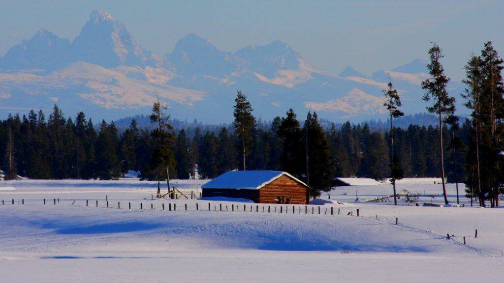 A red, historic building sits among the snow-covered fields in Harriman State Park with the Teton Range in the background.