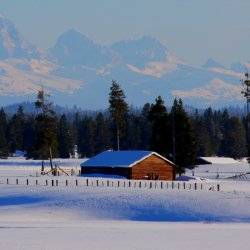 A red, historic building sits among the snow-covered fields in Harriman State Park with the Teton Range in the background.