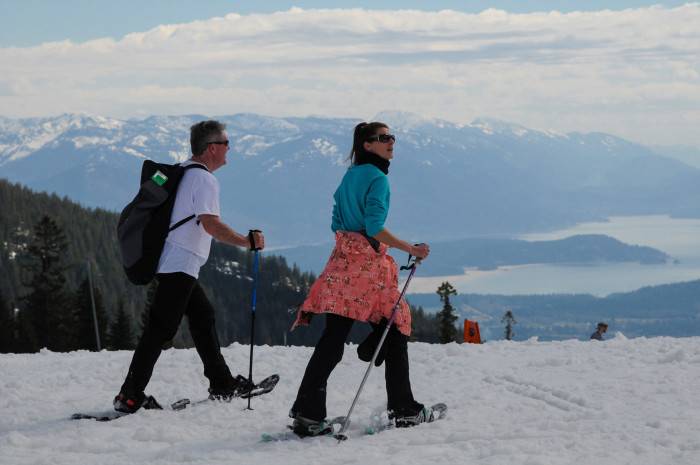 Male and female in short sleeves snowshoeing at Schweitzer Mountain with a view of Lake Pend Oreille below in the distance.