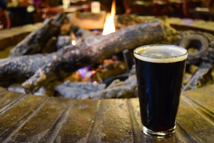 Dark beer sitting on the rim of a fire pit with a crackling fire in the background at Highlands Hollow in Boise.