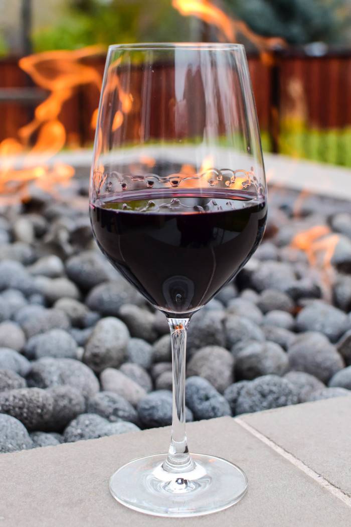 A glass of deep red wine sits in front of a glowing outdoor fire pit at Telaya Wine Co. and Coiled Wines in Boise..