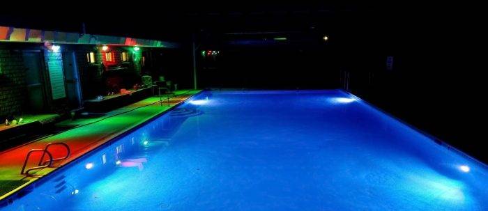 Outdoor heated pool glows blue whit green and red lights iluminating the surrounding deck.