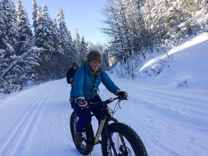 Closeup of woman on a fatbike riding on snow-covered trails with snowcovered trees in the background.