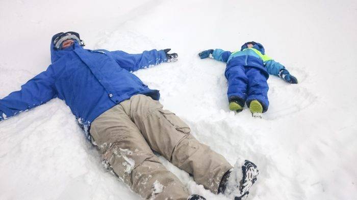 Father and sun on the ground making snow angels.