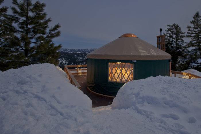 Green-sided yurt with a view of the valley and surrounded by snow.