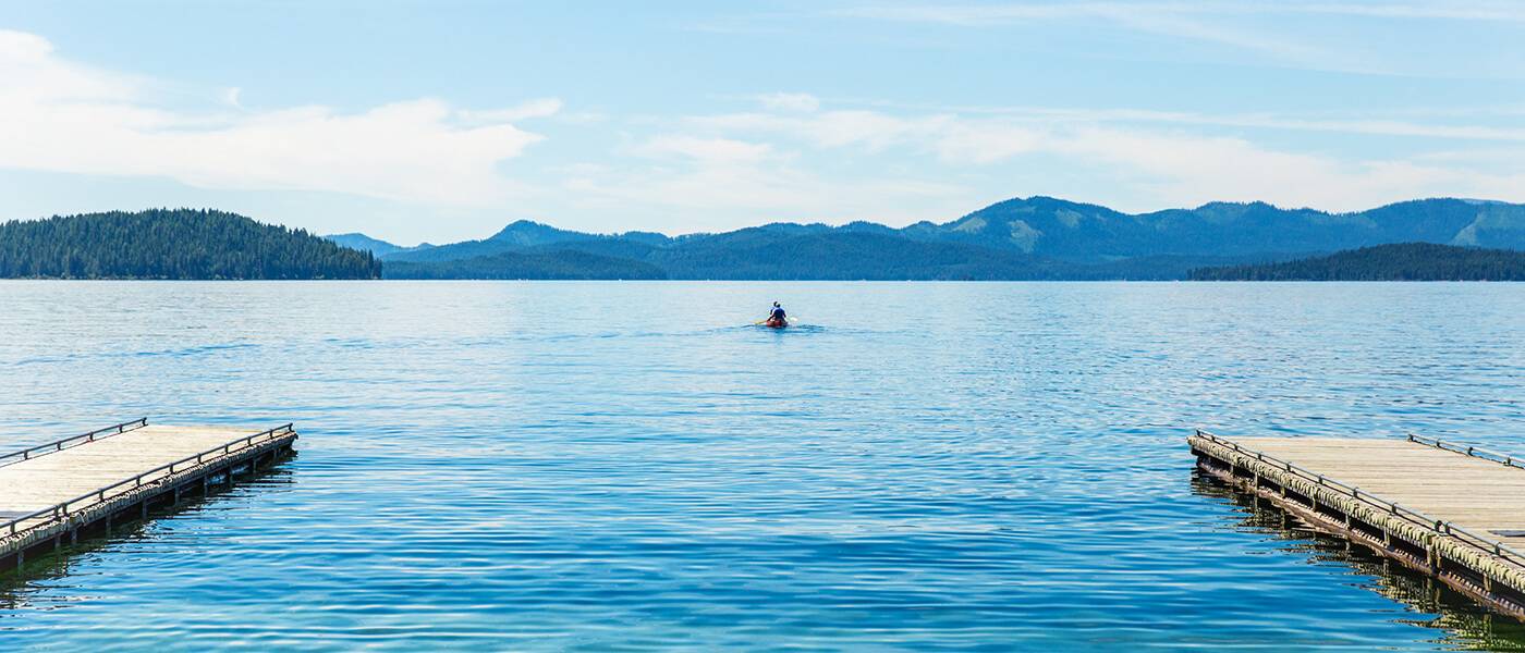 A sprawling view of Priest Lake at Priest Lake State Park, with two docks on either side and a person canoeing in the distance.