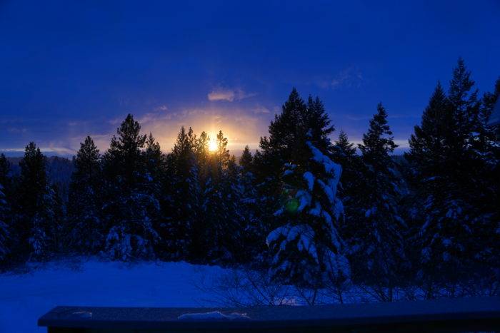 The sky is blue as darkness falls on the snowcovered ground and trees, with just a hint of brightness.