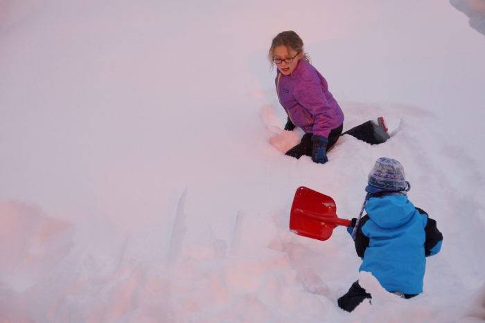 Young girl and boy with snow shovels play in the deep snow.