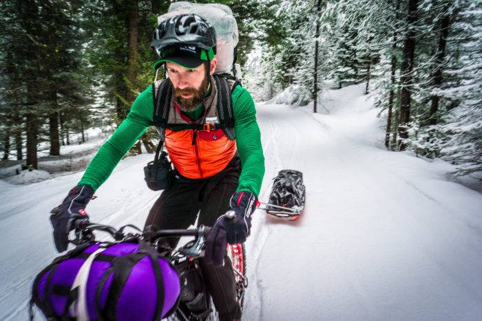 A man riding a fat bike pulling a sled through a snow-covered forest at Jug Mountain Ranch.