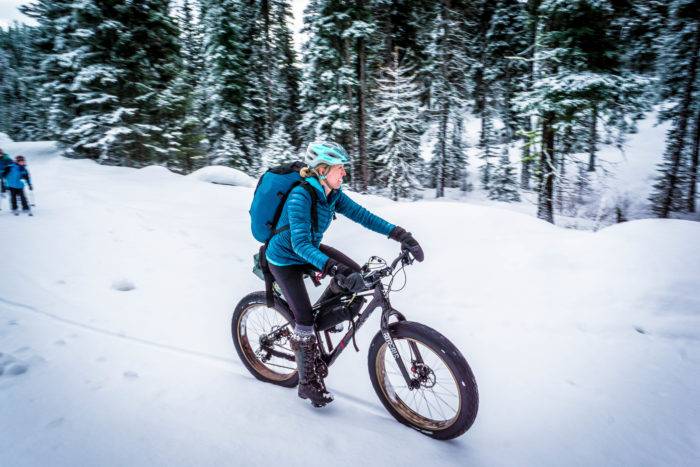 A woman riding a fat bike through a snowy forest of trees at Jug Mountain Ranch.