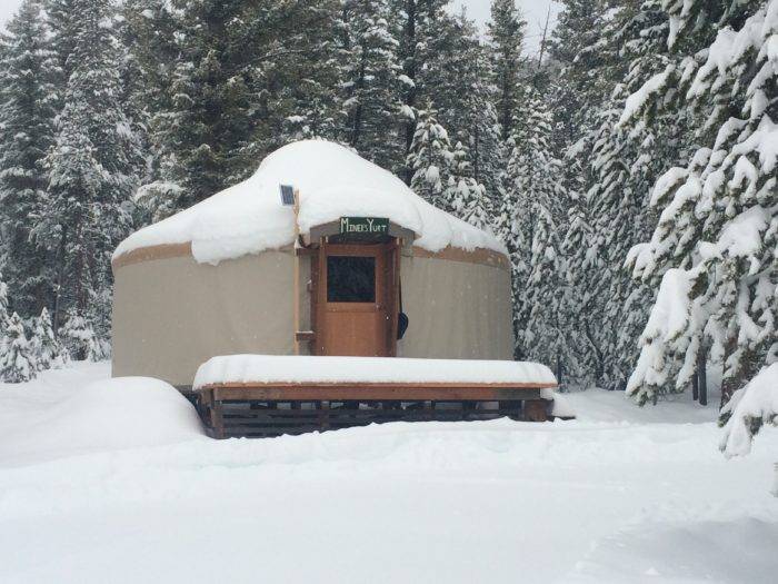 Snow-covered yurt surrounded by snow-covered trees.