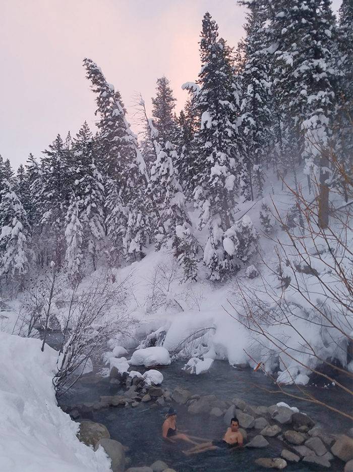 people sitting in hot pool along river in the snow