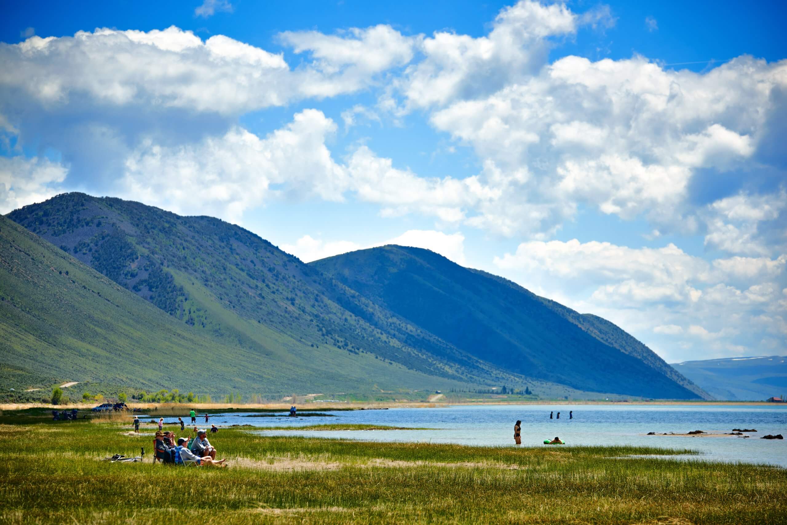 Various groups of people spend time in a park with mountains and a large lake.