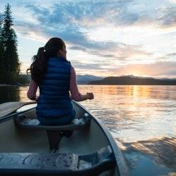 woman paddles canoe on lake at sunset