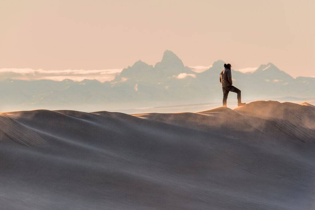 A man standing on sand dunes with mountain in background.