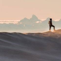 A man standing on sand dunes with mountain in background.