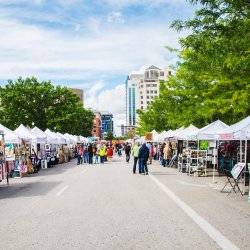 A street with two rows of tents selling various goods and several people walking around at the Capital City Public Market.