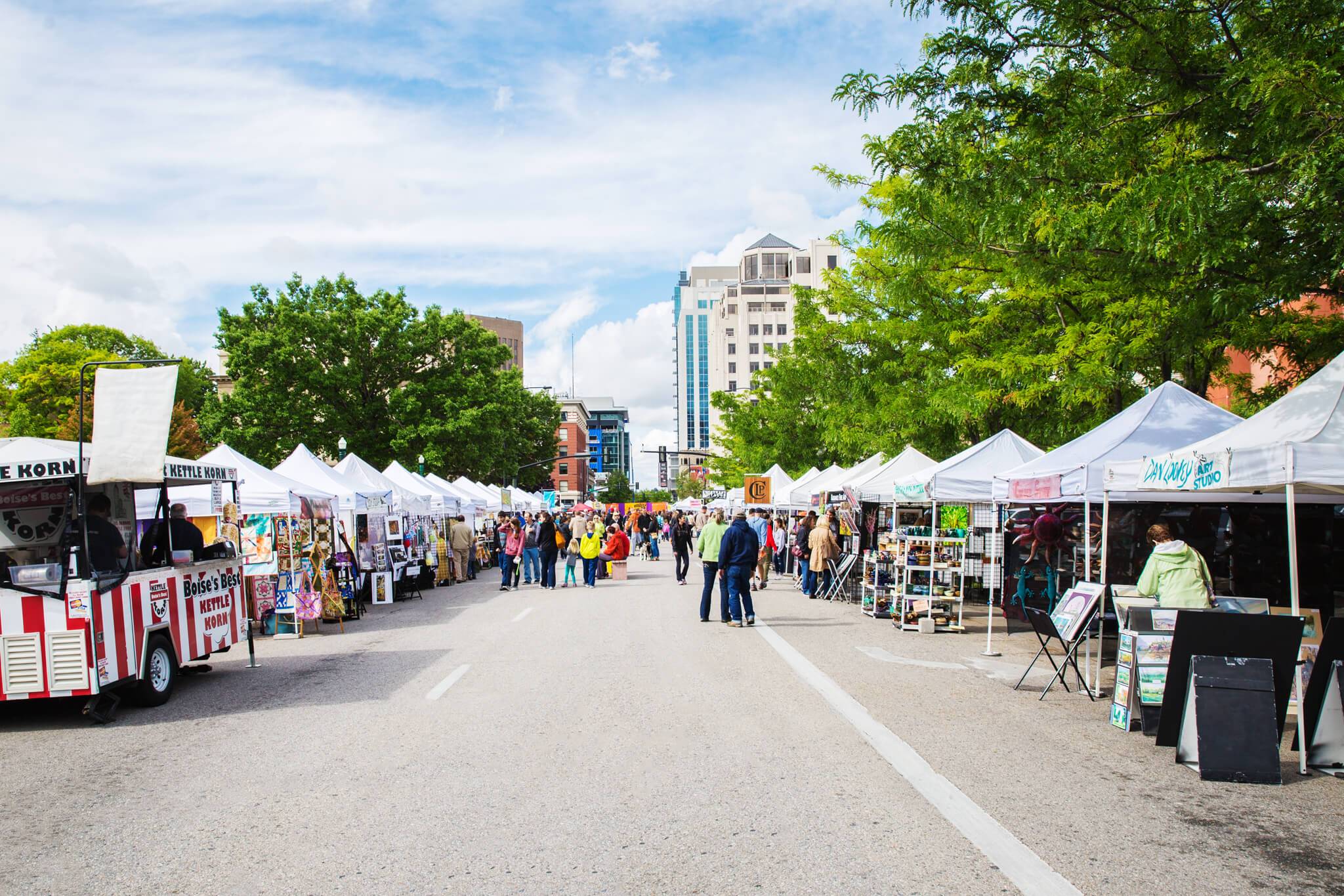 A street with two rows of tents selling various goods and several people walking around at the Capital City Public Market.