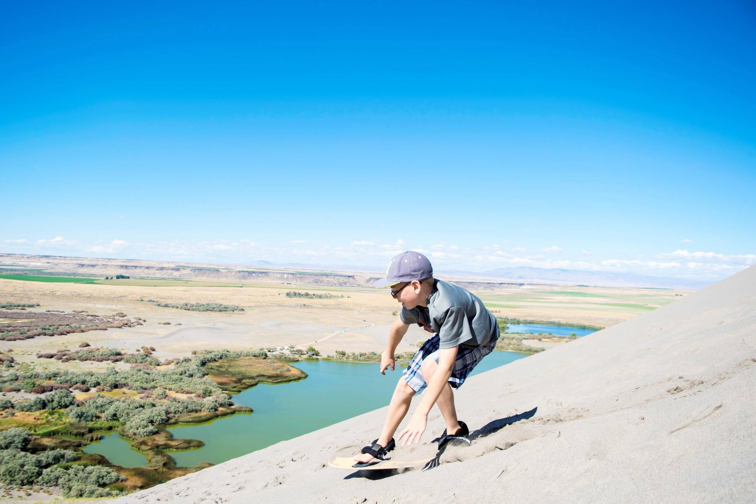 boy sandboarding down a sand dune