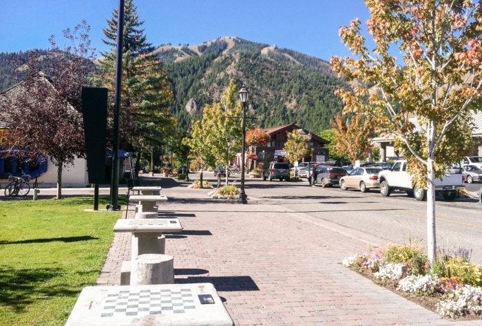 Tables cast shadows under fall trees as mountains overlook in the distance of Ketchum Town Square downtown. 