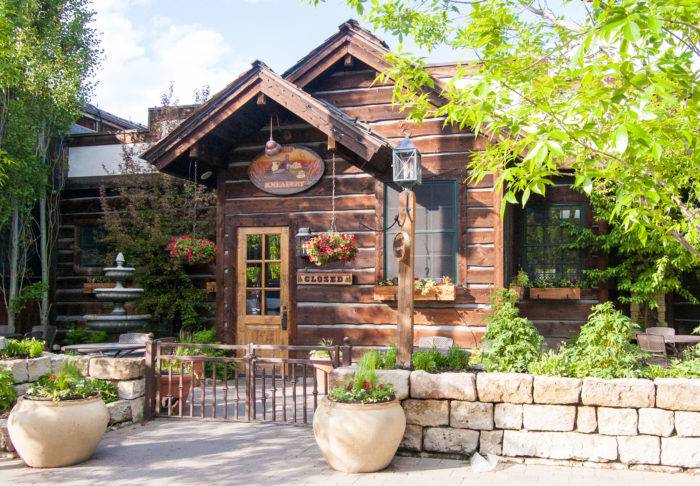 Trees and flower pots stand outside the exterior of The Kneadery, where the sign says, Closed.