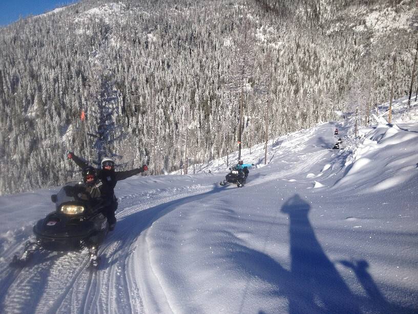 snowmobile riders enjoy a sunny trail ride in a Sandpoint valley.