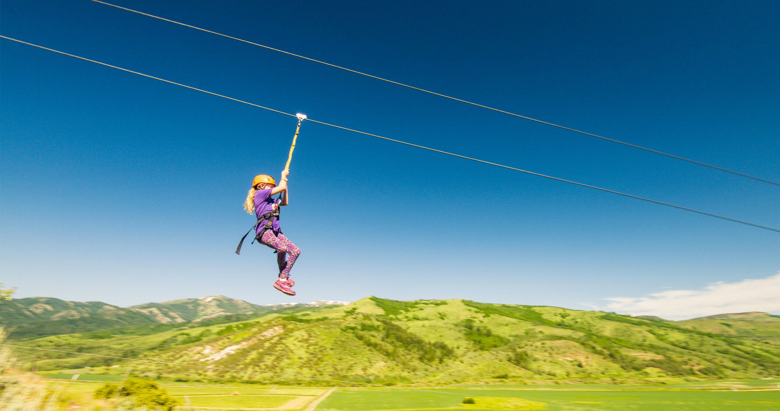 A girl ziplining at Lava Zipline Adventures with green mountains in the distance.