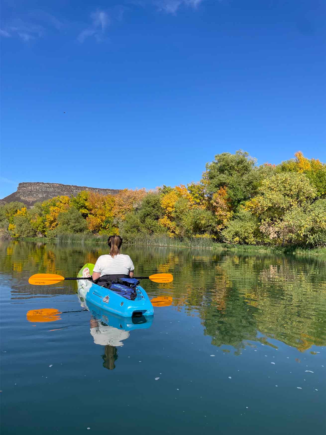 The colorful landscapes reflect in the waters as a kayaker paddles across the Blue Heart Springs.